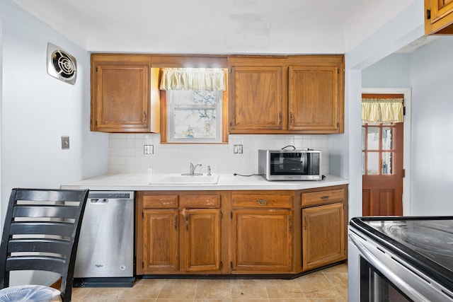 kitchen featuring brown cabinetry, appliances with stainless steel finishes, light countertops, and a sink