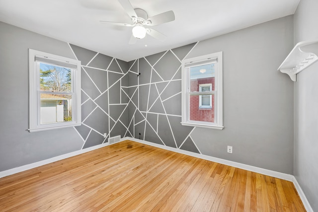 spare room with wood finished floors, visible vents, baseboards, a ceiling fan, and an accent wall