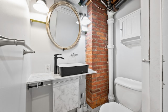 bathroom with brick wall, toilet, and vanity