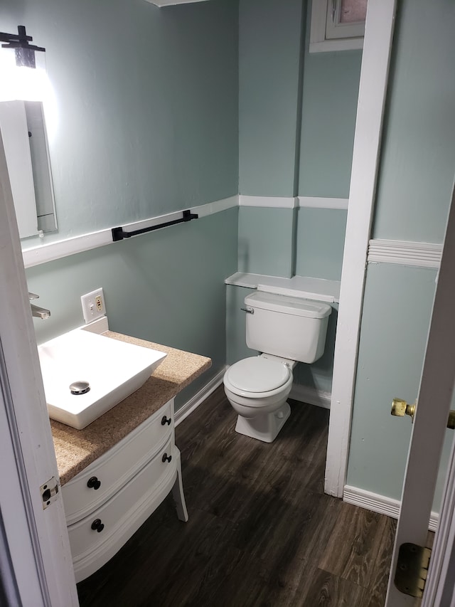 half bathroom with baseboards, toilet, wood finished floors, and vanity