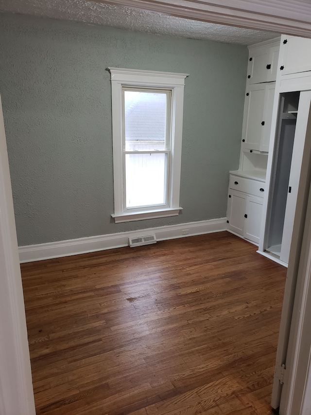 unfurnished bedroom featuring dark wood-style floors, visible vents, baseboards, a textured ceiling, and a textured wall