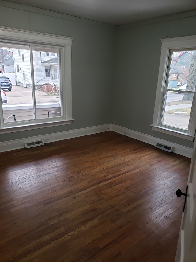 spare room featuring visible vents, crown molding, baseboards, and dark wood-style flooring