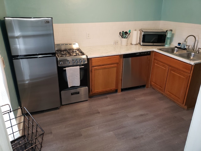 kitchen with tasteful backsplash, brown cabinets, appliances with stainless steel finishes, dark wood-style floors, and a sink