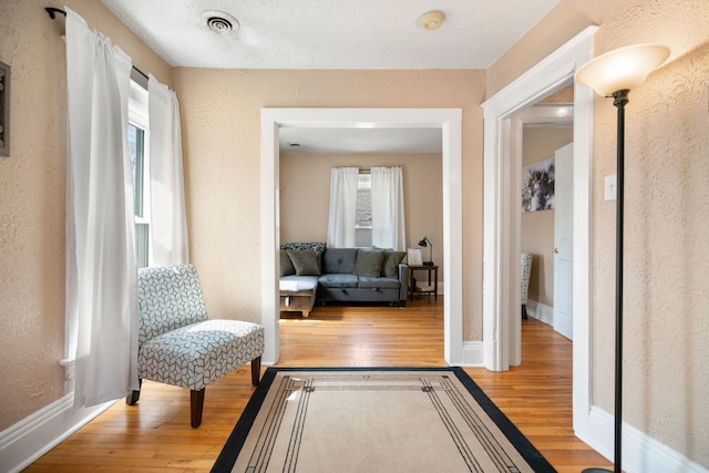 corridor featuring visible vents, hardwood / wood-style floors, and a textured wall