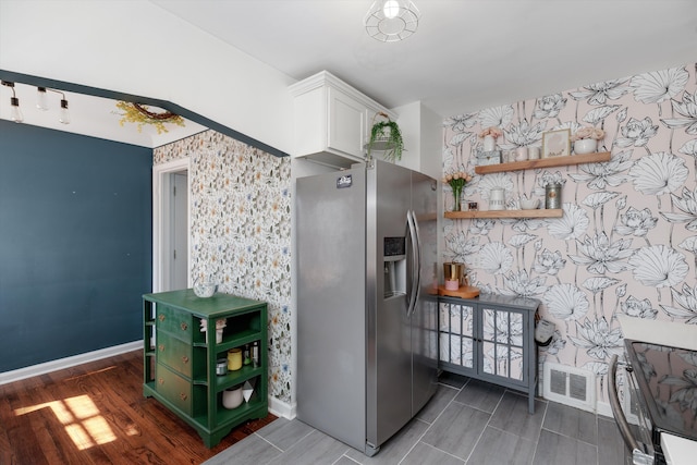 kitchen with stainless steel fridge, white cabinets, wallpapered walls, baseboards, and wood tiled floor