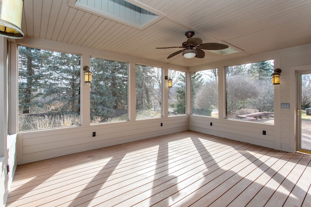 unfurnished sunroom featuring a ceiling fan, a skylight, wood ceiling, and a wealth of natural light