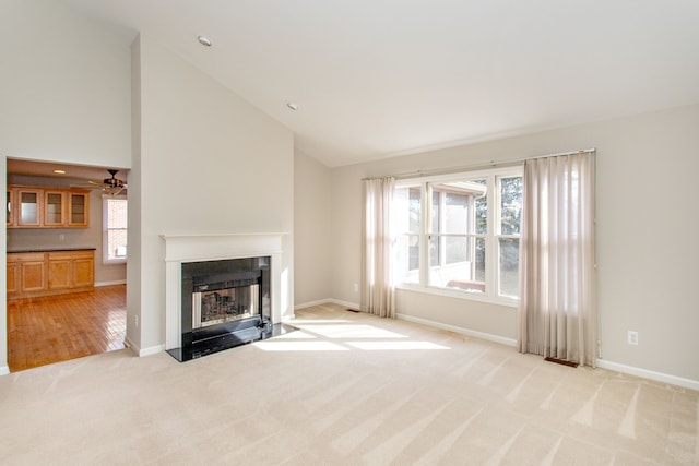 unfurnished living room featuring baseboards, a fireplace with flush hearth, high vaulted ceiling, and light carpet