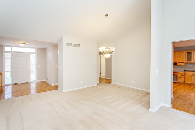 unfurnished dining area with visible vents, a notable chandelier, baseboards, light colored carpet, and a towering ceiling