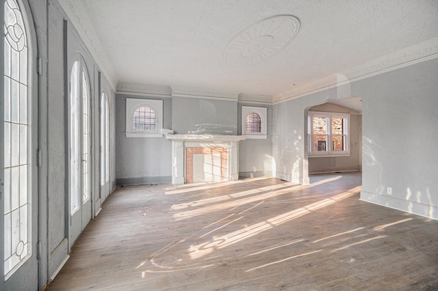 unfurnished living room featuring plenty of natural light, wood finished floors, a fireplace, and ornamental molding