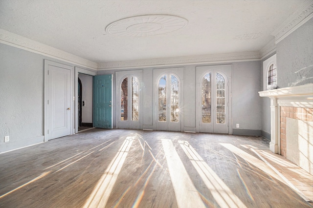 unfurnished living room with wood finished floors, baseboards, a textured ceiling, crown molding, and a textured wall