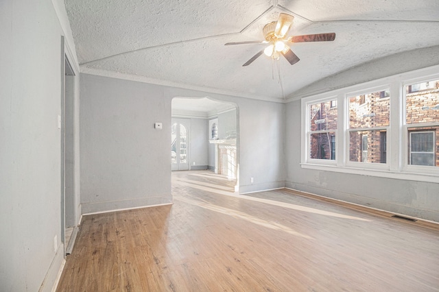 unfurnished room featuring a ceiling fan, a textured ceiling, wood finished floors, arched walkways, and lofted ceiling