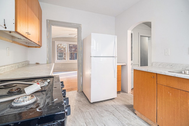 kitchen with a sink, freestanding refrigerator, range with gas cooktop, arched walkways, and light countertops