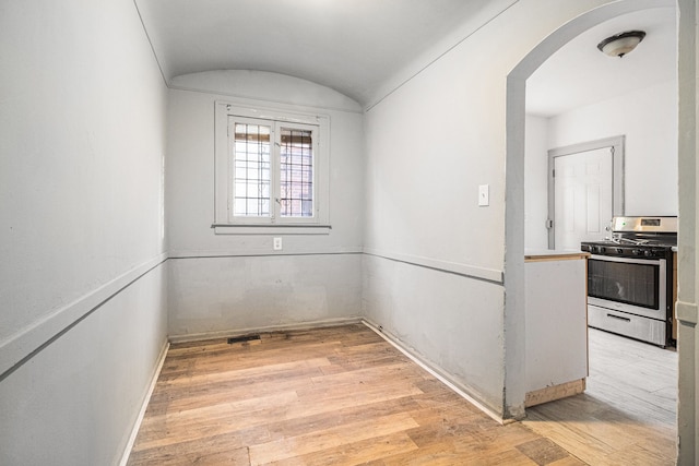 unfurnished room with light wood-type flooring, arched walkways, and lofted ceiling