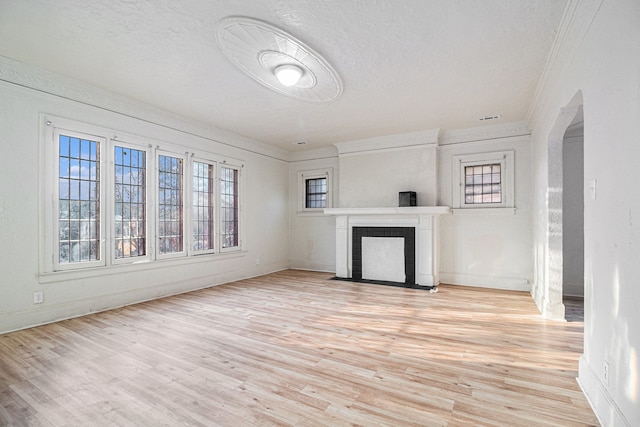 unfurnished living room with crown molding, a fireplace with flush hearth, light wood-type flooring, arched walkways, and a textured ceiling