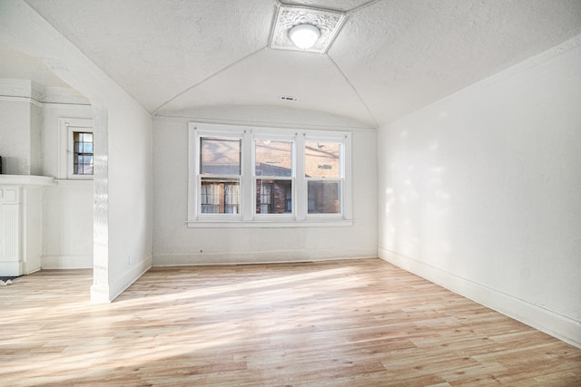 empty room featuring a wealth of natural light, light wood-type flooring, lofted ceiling, and baseboards