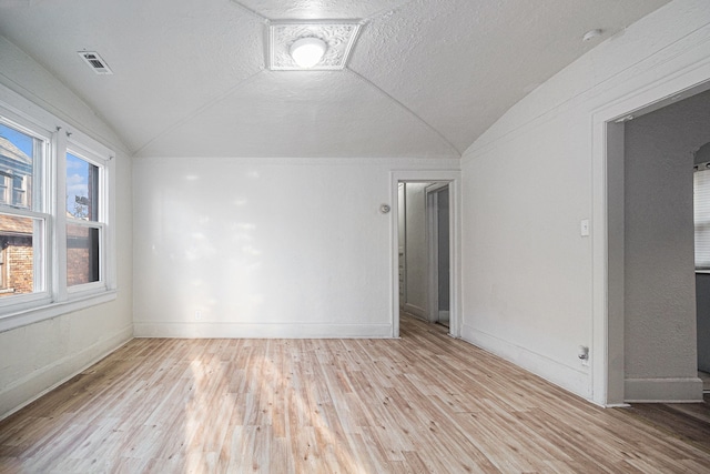 spare room with baseboards, lofted ceiling, a textured ceiling, and wood finished floors