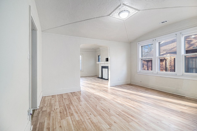 spare room with light wood-type flooring, visible vents, a textured ceiling, arched walkways, and lofted ceiling