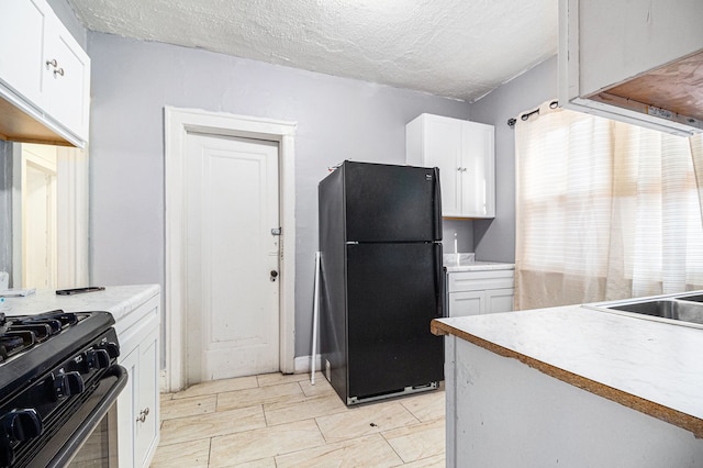 kitchen with a textured ceiling, white cabinetry, freestanding refrigerator, range with gas cooktop, and light countertops