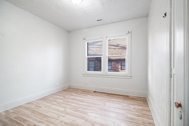 unfurnished room with baseboards, visible vents, light wood finished floors, and a textured ceiling