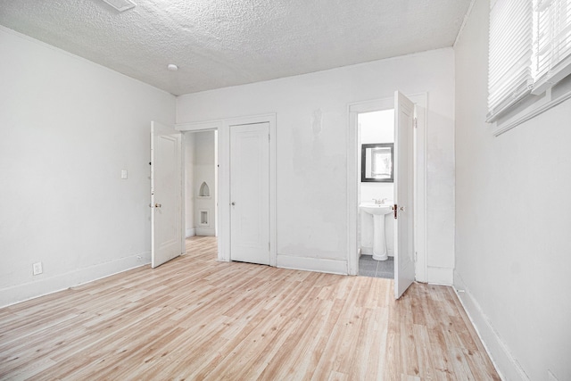 unfurnished bedroom featuring a sink, a textured ceiling, ensuite bath, wood finished floors, and baseboards