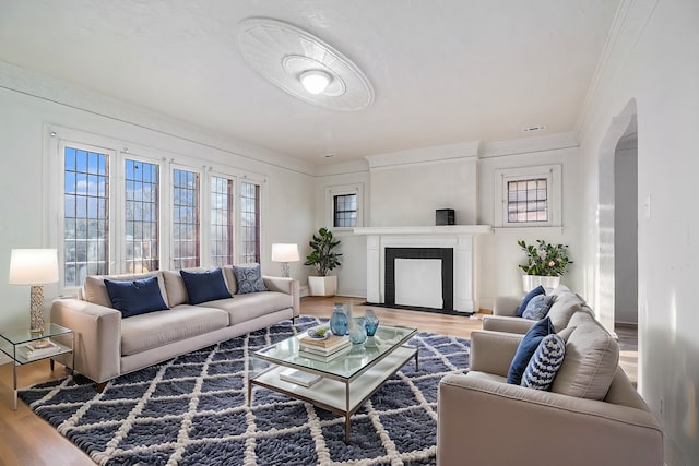 living area with arched walkways, a fireplace with flush hearth, ornamental molding, and wood finished floors