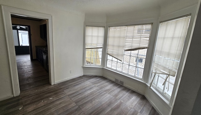 empty room with visible vents, a textured ceiling, baseboards, and wood finished floors