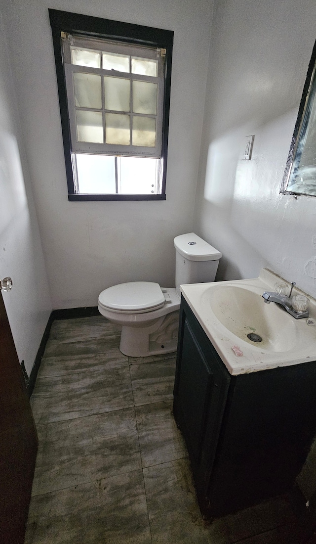 half bathroom featuring toilet, vanity, and baseboards