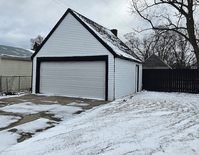 snow covered garage featuring a detached garage and fence