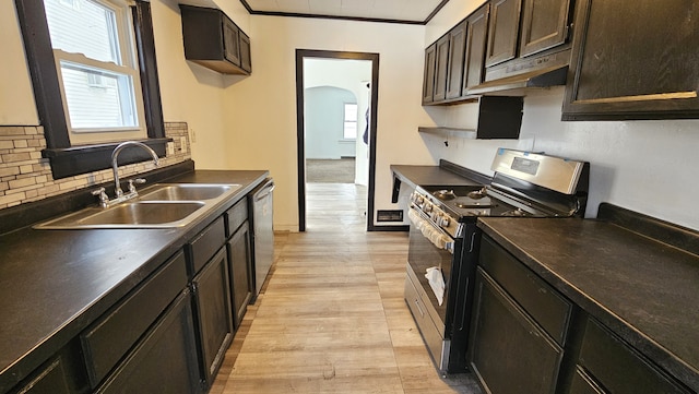 kitchen with dark countertops, under cabinet range hood, appliances with stainless steel finishes, arched walkways, and a sink