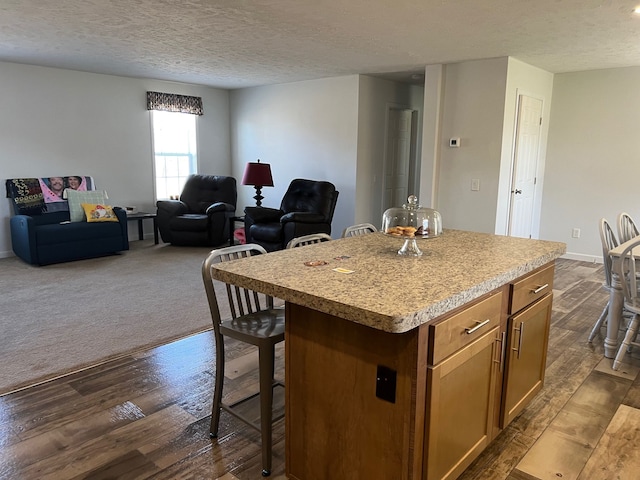 kitchen with dark wood-type flooring, a kitchen breakfast bar, a kitchen island, open floor plan, and light countertops