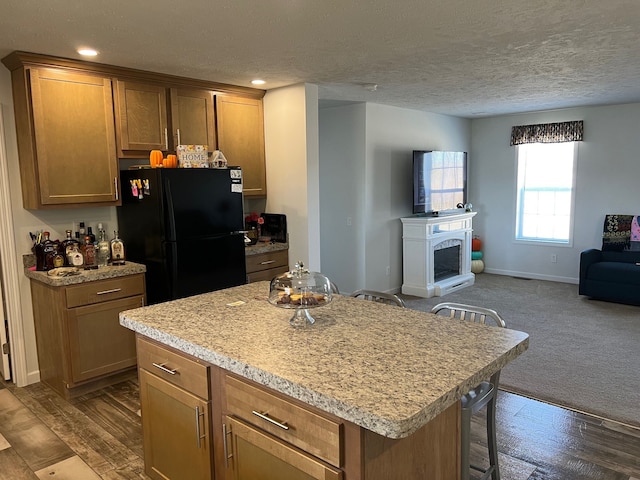 kitchen with a kitchen island, a fireplace with raised hearth, freestanding refrigerator, light countertops, and open floor plan