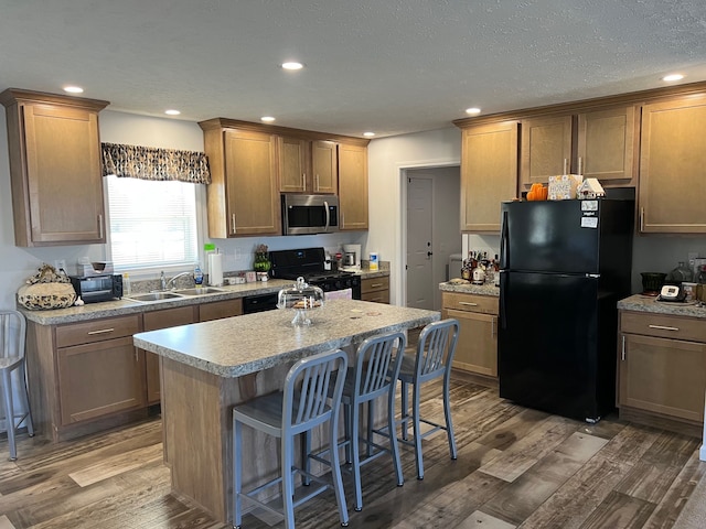 kitchen with black appliances, a sink, wood finished floors, a breakfast bar area, and light countertops