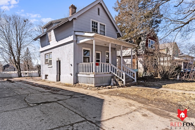 view of front facade featuring stucco siding, covered porch, and a chimney