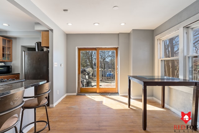 kitchen with glass insert cabinets, baseboards, black microwave, recessed lighting, and light wood-style flooring