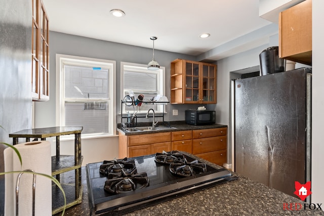 kitchen with glass insert cabinets, black microwave, freestanding refrigerator, brown cabinetry, and a sink