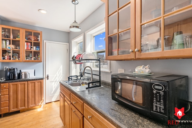 kitchen with dark countertops, black microwave, light wood-type flooring, brown cabinetry, and a sink