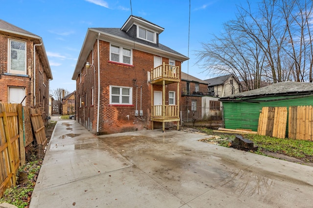 exterior space featuring brick siding, a patio, a balcony, and fence