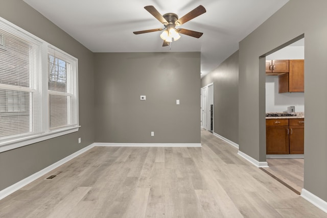 spare room with light wood finished floors, visible vents, a ceiling fan, and baseboards