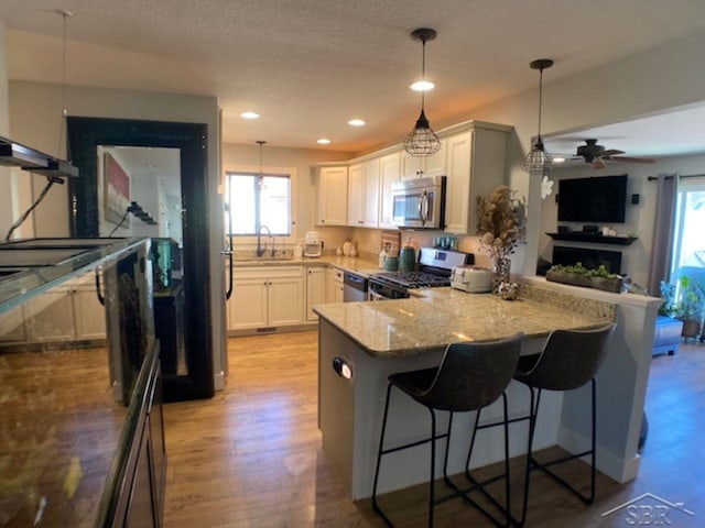 kitchen featuring a sink, decorative light fixtures, appliances with stainless steel finishes, and a peninsula