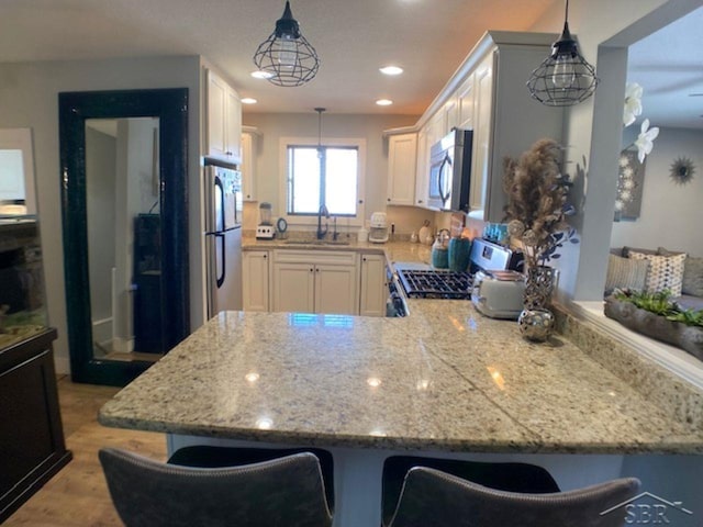 kitchen with light stone countertops, a peninsula, a sink, white cabinets, and appliances with stainless steel finishes