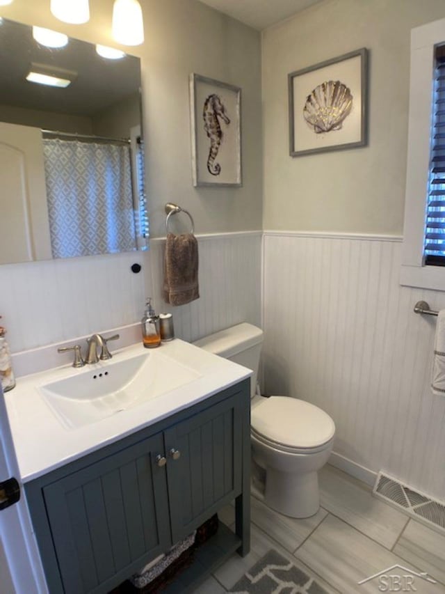 full bath featuring visible vents, curtained shower, toilet, wainscoting, and vanity