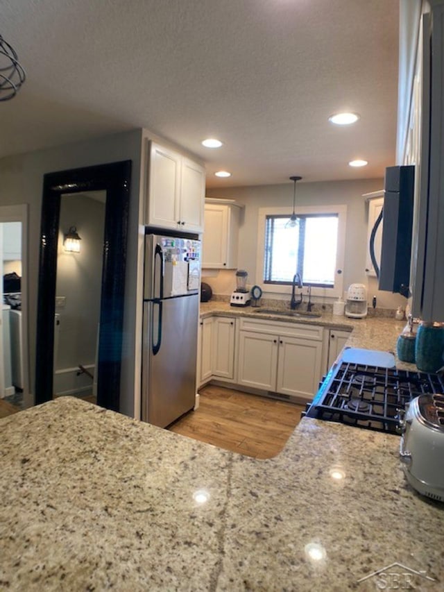 kitchen with white cabinets, light stone counters, freestanding refrigerator, and a sink