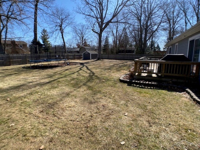 view of yard featuring a trampoline, a deck, an outdoor structure, a fenced backyard, and a storage unit