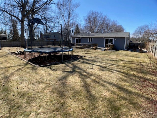 back of property featuring a wooden deck, a trampoline, a fenced backyard, and a lawn