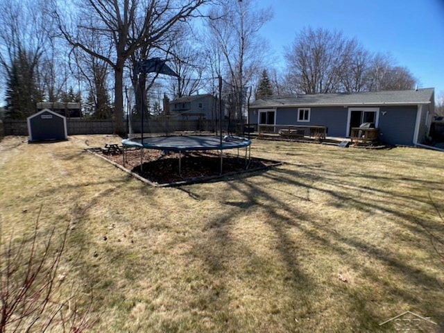 view of yard with a trampoline, fence, a shed, a wooden deck, and an outbuilding