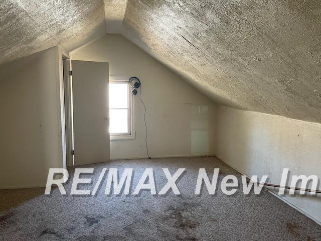 bonus room featuring lofted ceiling, carpet flooring, and a textured ceiling