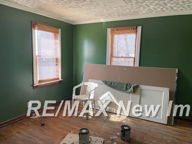 interior space featuring baseboards, a textured ceiling, wood finished floors, and ornamental molding