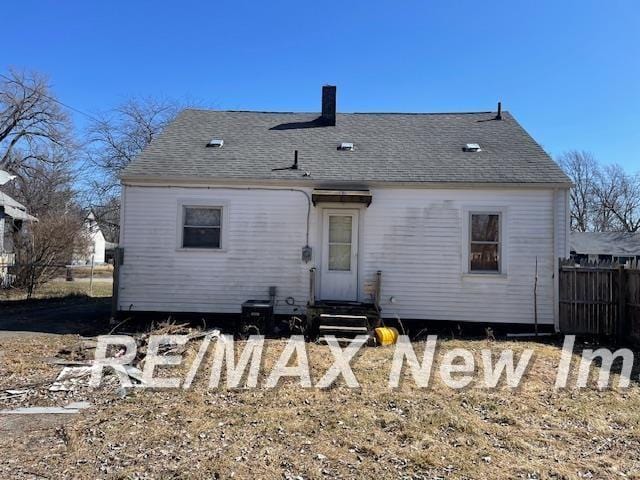 back of house with entry steps, roof with shingles, and fence