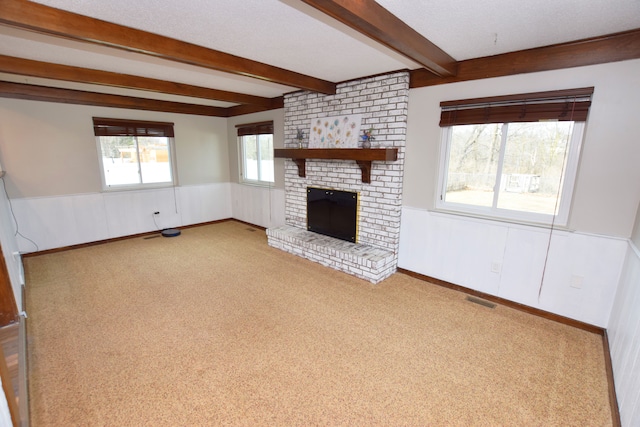 unfurnished living room with visible vents, carpet, beamed ceiling, wainscoting, and a fireplace