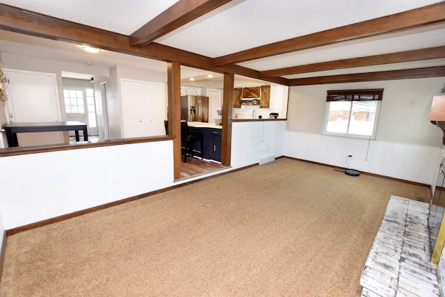 unfurnished living room with beamed ceiling, baseboards, carpet, and wainscoting